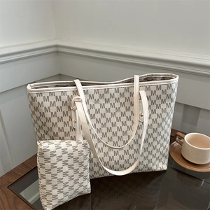 Large capacity beige monogram tote bag with matching pouch on a dark wood table