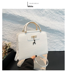 Detail of white crocodile pattern handbag with gold handle and deer charm