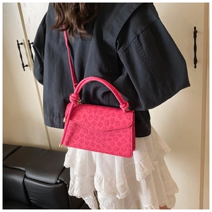 Detail of rose red square shoulder bag with four-leaf clover embossed pattern and knot handle
