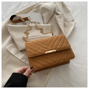 Macro detail of brown quilted suede flap bag with elegant V-stitch and gold chain
