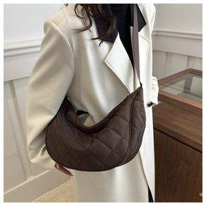 Détail du sac croissant matelassé marron foncé en nylon sur un manteau blanc