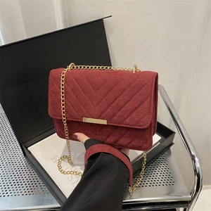 Burgundy suede shoulder bag with V-quilted pattern and gold chain strap in a lifestyle shot