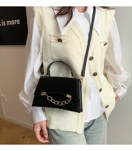 Detail view of a black leather box bag with gold chain and thin shoulder strap worn by model