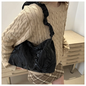 Detail of black glossy shoulder bag with textured surface and ruched strap on model