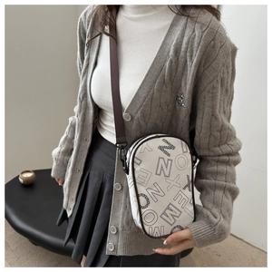 Detail of white crossbody bag with black lettering and dark brown textile shoulder strap