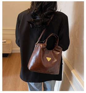 Detail of a dark brown glossy leather bucket bag with a golden triangular logo accent