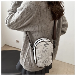 White crossbody bag with black lettering and adjustable strap worn by model in a sweater