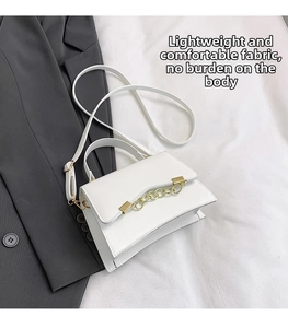 Detailed shot of white faux leather handbag with gold chain ornament on casual suit fabric