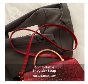 Detail of red crocodile texture handbag featuring a unique gold semi-circle metal handle