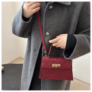 Close-up of burgundy suede handbag featuring a gold buckle and slim leather strap