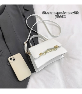 White mini crossbody bag with gold chain shown next to a phone for size comparison