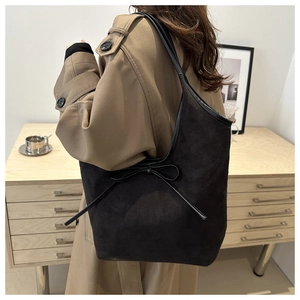 Minimalist black faux suede tote bag with a bow accent worn by a model in a warm room