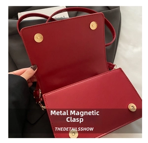 Macro view of gold magnetic snap closure on red leather textured crossbody bag
