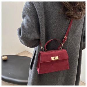 Détail du sac en daim bordeaux avec fermoir doré porté sur un manteau en laine gris