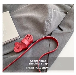Detail of red leather shoulder strap on grey wool fabric with stitching and round button