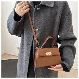 Détail d'un sac à main en daim marron avec fermoir doré porté sur un manteau en laine