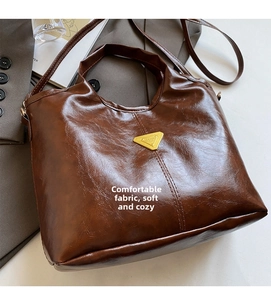 Detailed close-up of brown oiled leather texture and golden metal logo on bucket bag