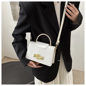 Detail of white lizard pattern handbag featuring a gold wavy clasp and metallic handle