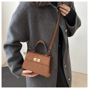 Macro view showing the soft suede texture and gold lock on the brown Kelly bag