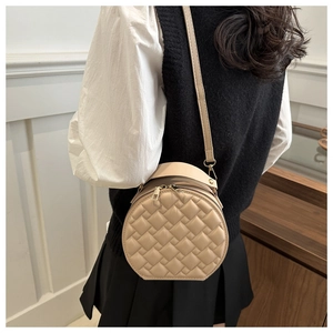 Detail view of a vintage beige quilted round crossbody bag worn by a model in a room