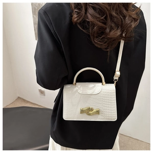Detail of white crocodile embossed mini bag with gold wave buckle on black suit jacket
