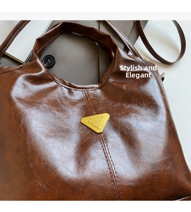 Macro view of dark brown oil wax leather handbag featuring gold triangular metal buckle