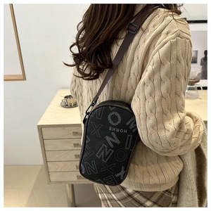 Vertical grey crossbody bag with white letter print and brown strap on a white sweater