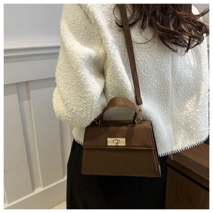 Sac à main en daim marron givré avec fermoir doré porté par un mannequin de mode