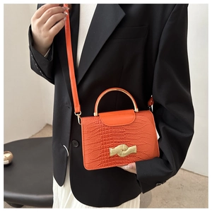Detail of bright orange crocodile pattern leather bag with curved gold metal handle