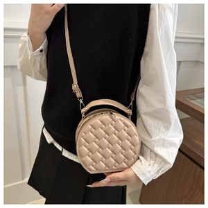 Detail of beige round crossbody bag with woven texture and gold hardware on model