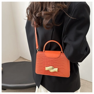 Detail view of an orange crocodile texture crossbody bag with wavy gold buckle and handle