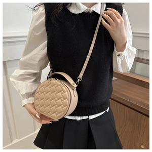 Detail of a beige quilted round crossbody bag with gold hardware and top handle