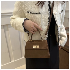 Détail d'un sac à main Kelly en daim marron foncé avec fermoir doré sur un manteau