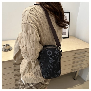 Close-up of black crossbody bag with white letter print on model in a cozy interior
