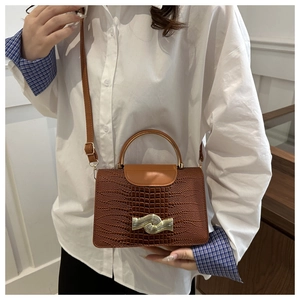 Detail of a brown crocodile pattern handbag with a golden arch handle and metal buckle