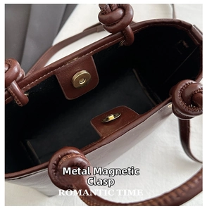Detail of dark brown leather bucket bag featuring a gold magnetic clasp and knot handle