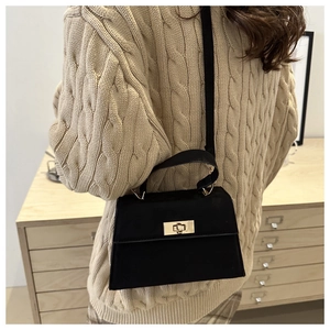 Détail d'un sac à main Kelly noir vintage avec fermoir doré sur un pull en maille beige