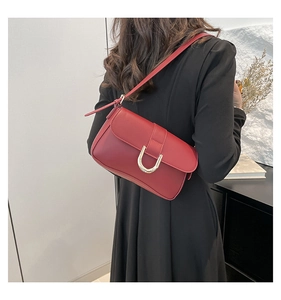Detail of red faux leather baguette bag with gold horseshoe buckle on model's shoulder