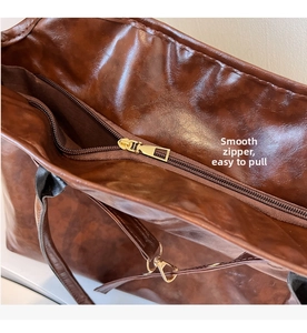 Close-up of smooth gold zipper closure and textured brown leather on large tote bag