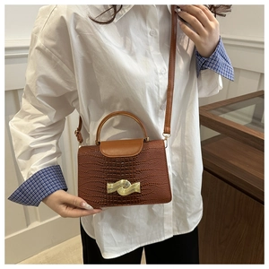 Detail of brown crocodile pattern crossbody bag featuring a wavy golden metal clasp