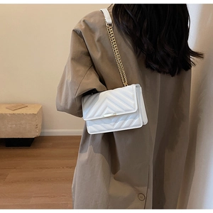Chic white V-quilted shoulder bag with gold hardware worn by a model in a cozy room