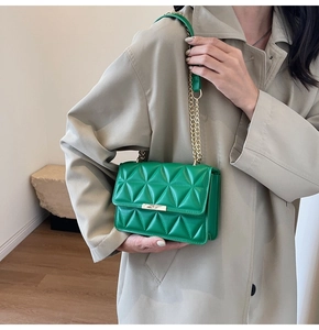 Detail of green quilted crossbody bag with gold chain strap and metal lock closure