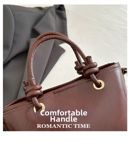 Close-up of brown leather handbag handle with knotted rope design and gold metal grommets