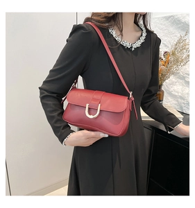 Detail of red minimalist crossbody bag with gold U-shaped buckle on black dress