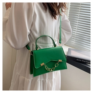 Detail of green crossbody box bag with gold chain and irregular flap design