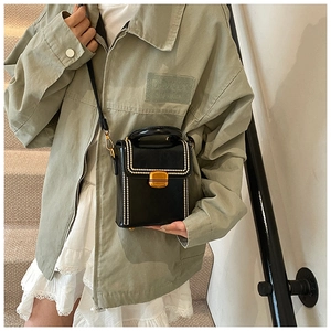 Detail of elegant black box bag with white pearl trim and gold clasp lock on model