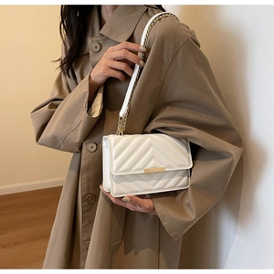 Quilted white crossbody bag with gold metallic lock and chain strap on a trench coat
