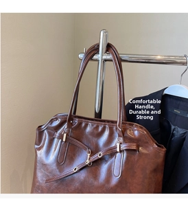 Detail of dark brown tote bag with metallic buckle and long straps on a black blazer