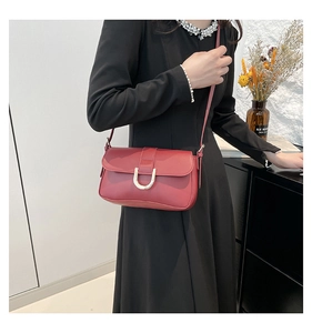 Detail view of burgundy leather shoulder bag with gold U-shaped buckle on a model