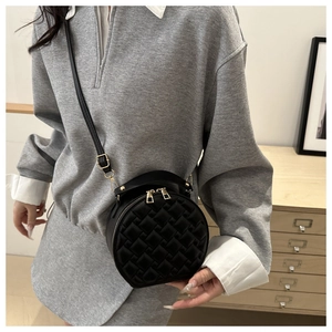 Detailed close-up of a black circular crossbody bag with woven texture and gold zippers